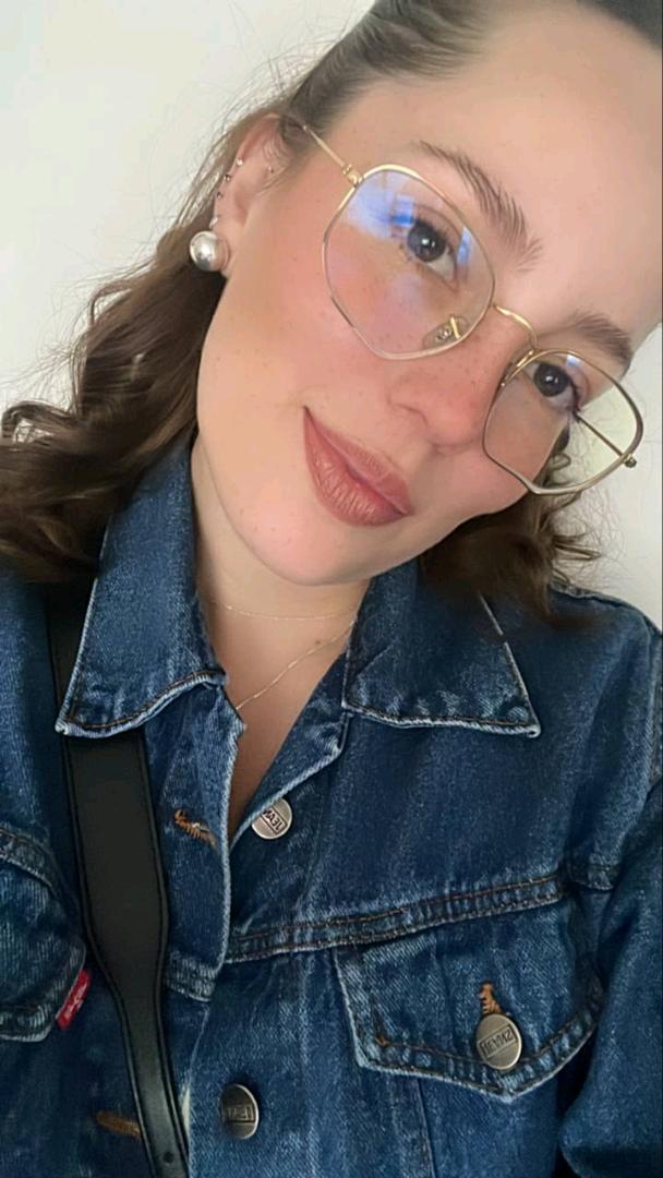 Woman in glasses and a denim jacket looking into her front camera