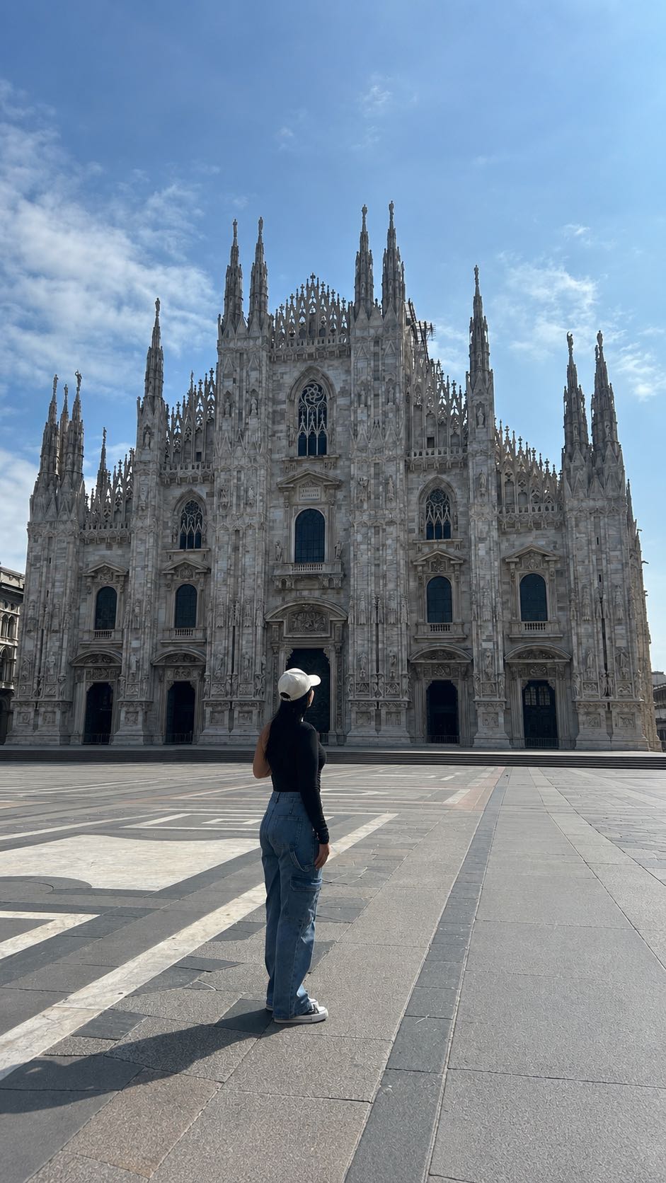 Woman standing in a sunny city square in front of a gothic cathedral